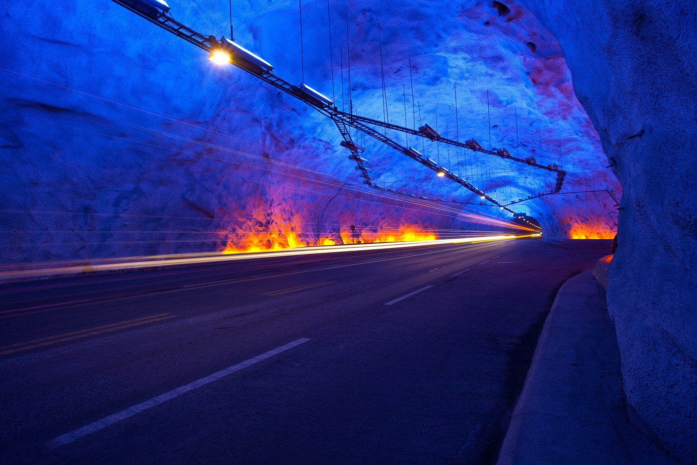 Interior of the Lærdal Tunnel in Norway, a drill-and-blast road tunnel, showing exposed rock and a single carriageway.